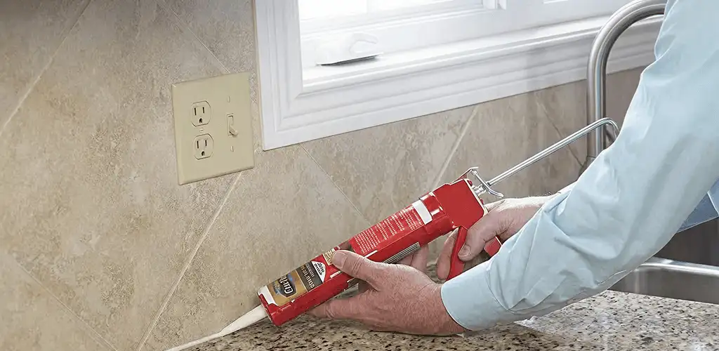Handyman applying caulk along a kitchen backsplash and countertop seam in Syracuse, NY